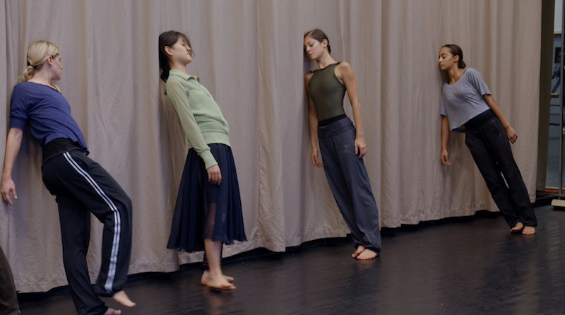 Four dancers from the Paris Opera Ballet in practice clothes lean their heads and shoulders on a wall.